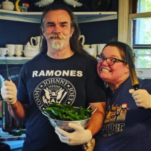 John and Jenn wearing rubber gloves and holding knives, ready to cut a bowl of jalapenos for canning. John looks calm, but Jenn has a demented smile.